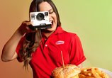 A woman in a Denny's uniform takes a photo of a Denny's meal with the Denny's Rewards logo in the background