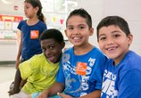 Four kids smiling and looking at the camera while wearing orange No Kid Hungry stickers