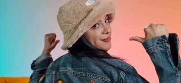 A woman in a denim jacket and fur hat showing a sign on her back