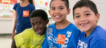 Four kids smiling and looking at the camera while wearing orange No Kid Hungry stickers
