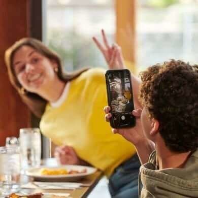 A man taking a photo of a smiling woman at Denny's